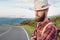 Portrait of a bearded happy serious traveler hipster with a backpack in a plaid shirt and a hat next to an unknown car