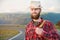 Portrait of a bearded happy smiling traveler hipster with a backpack in a plaid shirt and a hat next to an unknown car