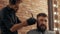 Portrait bearded man getting haircut in barbershop. Hairstylist cutting hair with electric razor in male salon. Close up