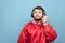 Portrait of a bearded man in his headphones and a red jacket on a blue background, looking in camera. Adult man listens to music