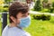 Portrait of a bearded man in protective blue medical mask against a blurred outdoor background. Male in a respirator