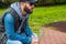 Portrait of a bearded man with sunglasses and hat sit on bench in a park