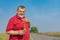 Portrait of bearded Ukrainian senior man holding and looking on young sunflower while standing on a country road