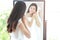 Portrait of beautiful Asian bride put on earring looking in mirror, her back out of focus large copy space, horizontal layout and