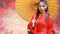 Portrait of beautiful asian woman wearing a red warrior Chinese costume with an ancient umbrella and black ancient sword. She stan