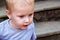 Portrait of beautiful baby boy outside. Adorable kid looks with interest at something sitting on the stair.