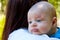 Portrait of beautiful baby in loving mother`s arms, newborn head is resting on the shoulder to burp, cute infant face close up