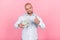 Portrait of a beautiful bald man with a beard dressed in a white shirt. holds a bucket of dollars and shows a thumbs up sign stand