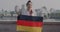 Portrait of beautiful biracial girl waving German national flag and smiling standing in modern city