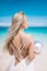 Portrait of the beautiful blond long hair bride in a open back wedding dress stand on the white sand beach with a pearl.