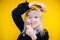 Portrait of beautiful blonde girl in a black jacket smiling and holding her hair against a background of yellow wall. Funny face.