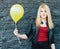 Portrait of a beautiful blonde girl near a black brick wall with a yellow balloon with warm sunny day