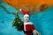 Portrait of a beautiful boy underwater in a Santa Claus costume at the bottom of the pool. He is holding a Christmas