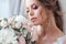 Portrait of beautiful bride. Blonde bride sits on a white bed and sniffs a bouquet.