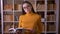 Portrait of beautiful brunette teacher in glasses reading book at the library turns to camera and smiles.