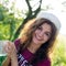 portrait of beautiful brunette young woman in white hipster hat happy smiling holding glass cup of water on green summe