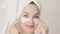 Portrait of beautiful Caucasian young woman with hair wrapped in white towel, applying facial clay mask touching her