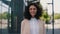 Portrait of the beautiful curly smiling young businesswoman in formal outfit standing near the business centre looking