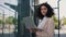 Portrait of the beautiful curly smiling young businesswoman in formal outfit standing near the business centre looking