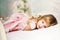 Portrait of beautiful cute little 3 years old blond girl with blue eyes lying on bed in pink dress. Moment of relaxation for