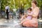 Portrait of beautiful disabled girl in the arms of his mother having fun in fountain of public park at sunny summer day. Child