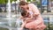 Portrait of beautiful disabled girl in the arms of his mother having fun in fountain of public park at sunny summer day. Child cer