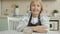 Portrait of beautiful elderly woman wearing apron sitting in kitchen alone and looking at camera