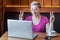 Portrait of beautiful emotional positive girl with blonde short hair in pink t-shirt is sitting in cafe and working on laptop with