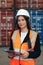 Portrait of beautiful engineer woman with walkie-talkie in white helmet and vest working in container terminal port