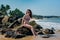 Portrait of a beautiful exited european girl in bikini sitting on the rocks on the beach