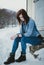 Portrait of beautiful fashion model posing to camera and sitting on the stone in front the caravan in winter time. Full body shot