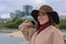 Portrait of a beautiful fashionable young woman in a hat and coat on the riverfront in the city.