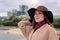 Portrait of a beautiful fashionable young woman in a hat and coat on the riverfront in the city.