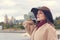 Portrait of a beautiful fashionable young woman in a hat and coat on the riverfront in the city.