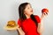 Portrait of a beautiful fat girl in surprise and holding a red apple and a hamburger, on gray background