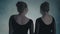 Portrait of beautiful female twins standing with their backs to the camera and sharply turning their faces and looking
