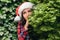 Portrait of a beautiful girl with a dreaming, piercing look in a santa claus red hat looks away through green branches of juniper.