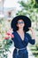 Portrait of a beautiful girl in a hat and glasses on the street near blooming roses