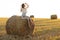 Portrait of beautiful girl on haystack roll on harvested wheat field in the summer. Selective focus