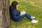 Portrait of a beautiful girl with a mask sitting under a sturdy tree with a book to relax and have peace of mind in times of