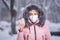 Portrait of a beautiful girl in a pink jacket in a medical protective mask in holding pills in her hands for colds and flu. Winter