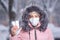 Portrait of a beautiful girl in a pink jacket in a medical protective mask in holding white pills in her hands for colds and flu.