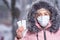 Portrait of a beautiful girl in a pink jacket in a medical protective mask in holding white pills in her hands for colds and flu.