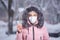 Portrait of a beautiful girl in a pink jacket in a medical protective mask in holding yellow pills in her hands for colds and flu