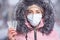 Portrait of a beautiful girl in a pink jacket in a medical protective mask in holding yellow pills in her hands for colds and flu