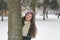 Portrait of beautiful girl in the snow hiding behind a tree.