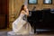 Portrait of a beautiful girl wearing white wedding dress sitting at the piano and dreaming