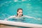 Portrait of a beautiful girl with wet hair floating in the pool, wearing a white shirt. Rest in the water in hot weather