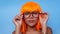 Portrait of beautiful happy Asian woman in bright orange wig and glasses posing over blue