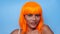 Portrait of beautiful happy Asian woman in bright orange wig posing over blue